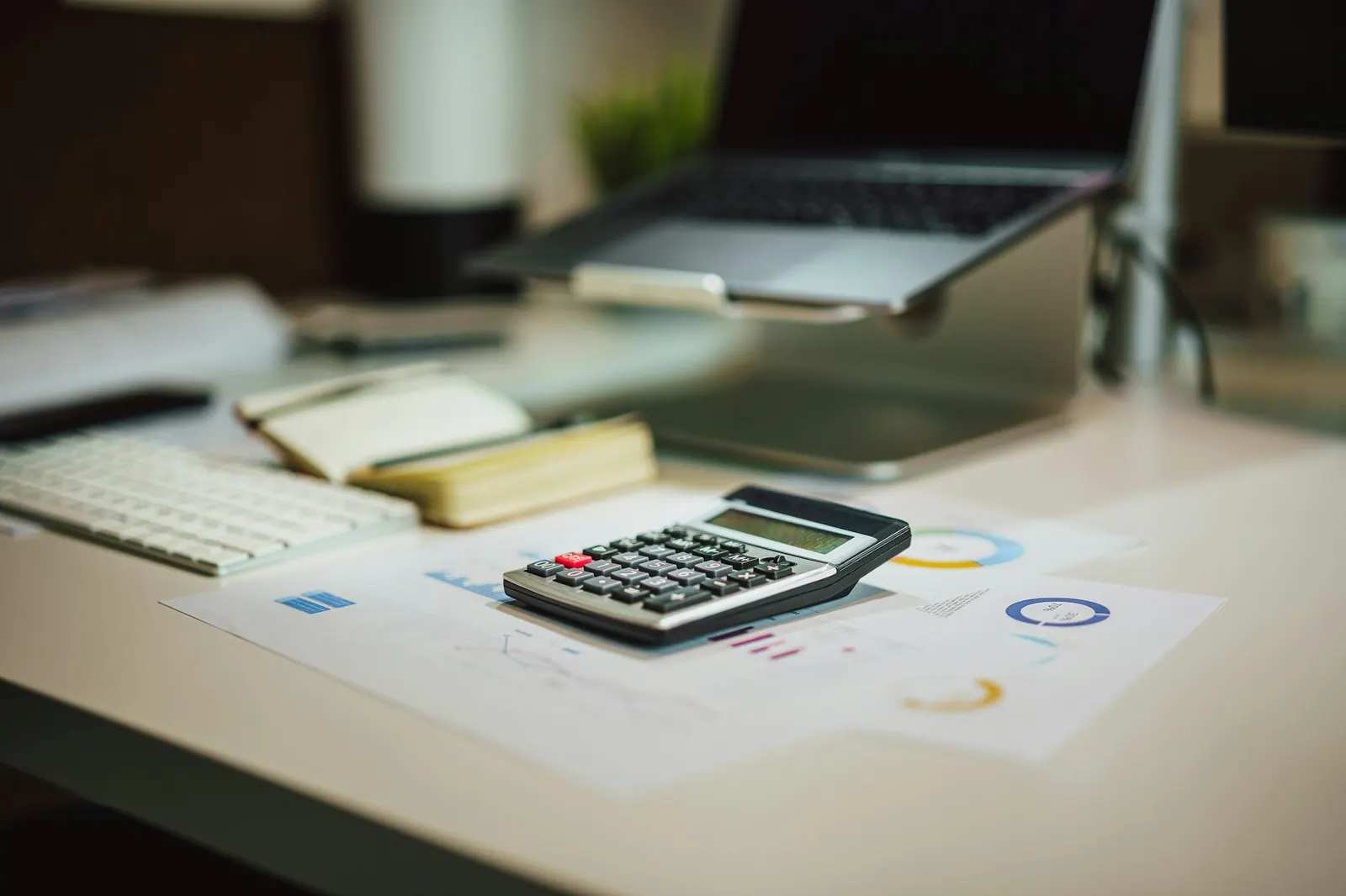 A tidy accounting desk with a calculator, reports and a laptop